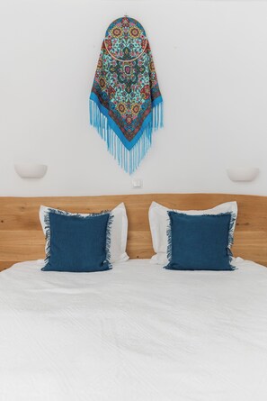 A bed with a white sheet, two blue pillows, and a colorful patterned throw blanket hanging above. - 5chirpici (Murighiol)