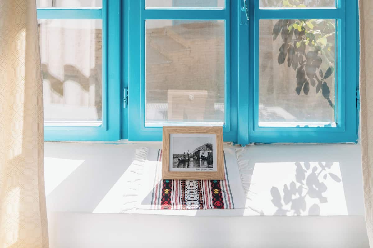 A room with a large window, a framed picture on the windowsill, and a curtain.