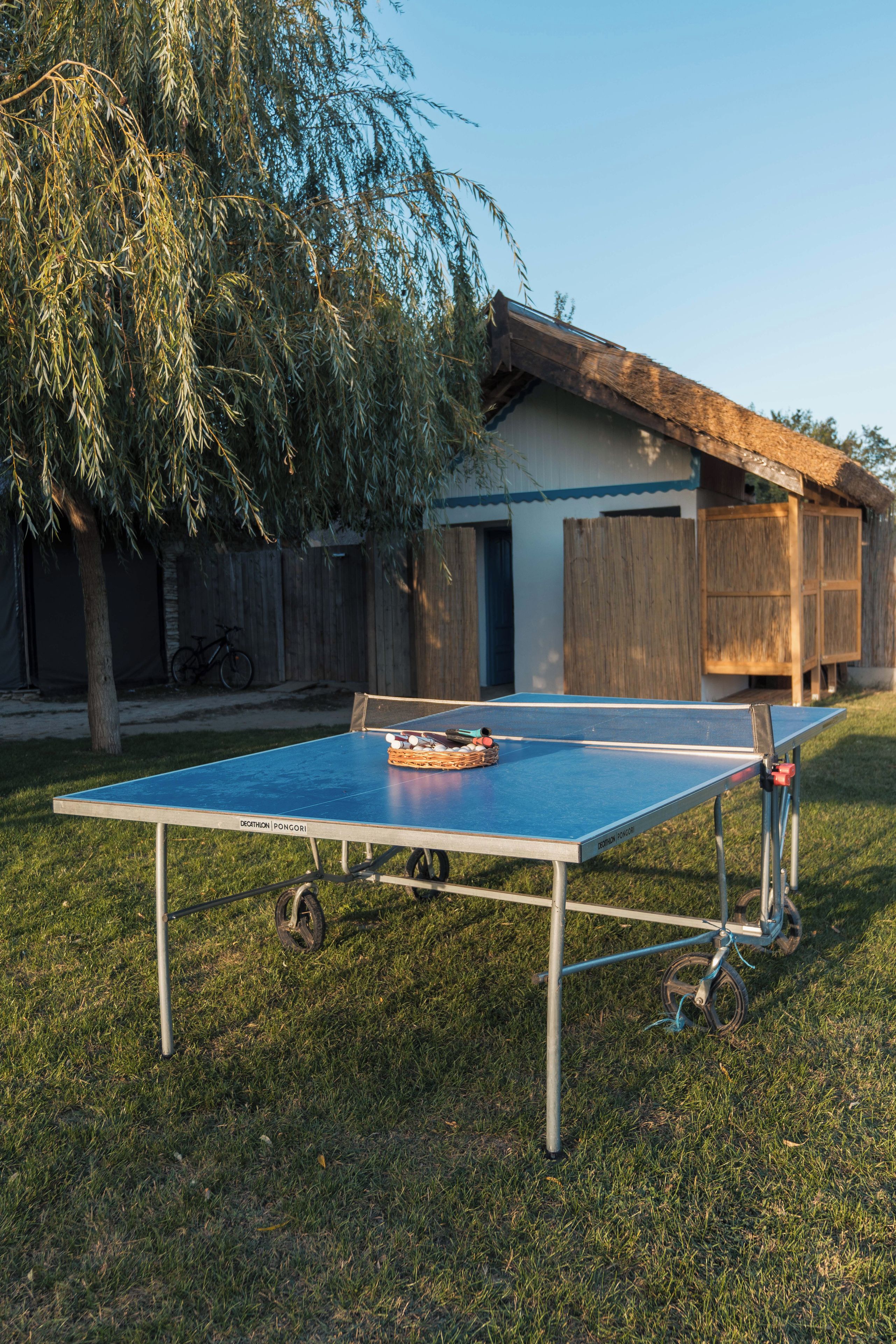 A ping pong table set up outdoors with a bicycle nearby.