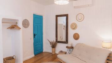 A room with a blue door, a round woven rug, a sofa, a mirror, and wall-mounted hats.