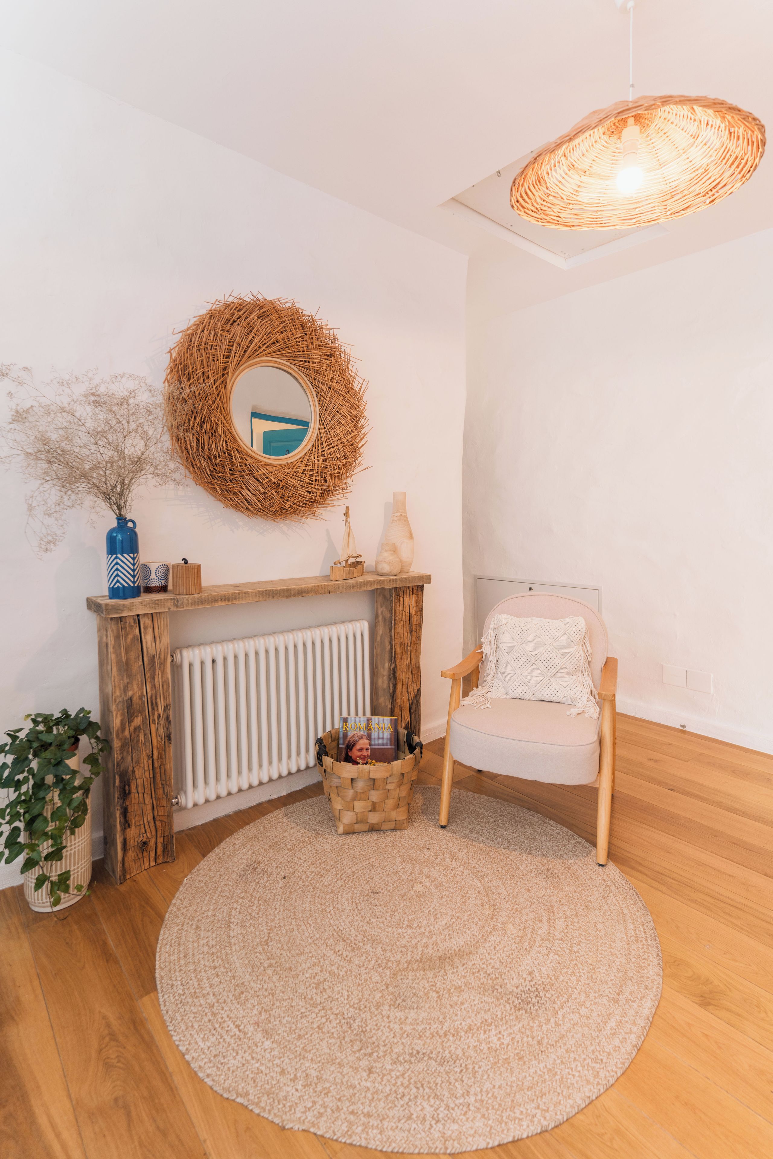 A room with a round rug, a wooden chair, a wicker wall hanging, a white radiator, and a blue vase.