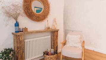 A room with a round rug, a wooden chair, a wicker wall hanging, a white radiator, and a blue vase.