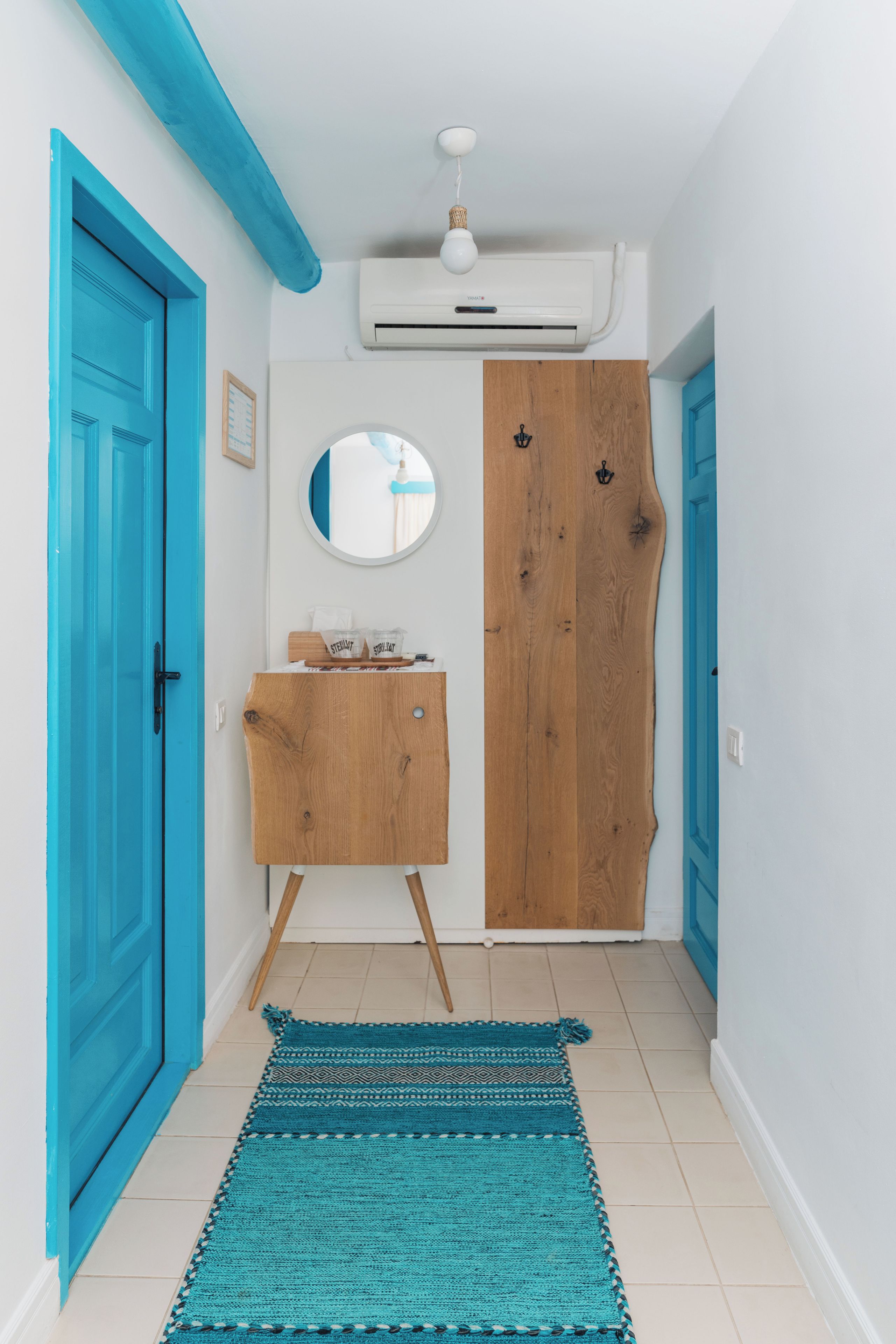 A hallway with a wooden cabinet, a round mirror, and a teal rug.