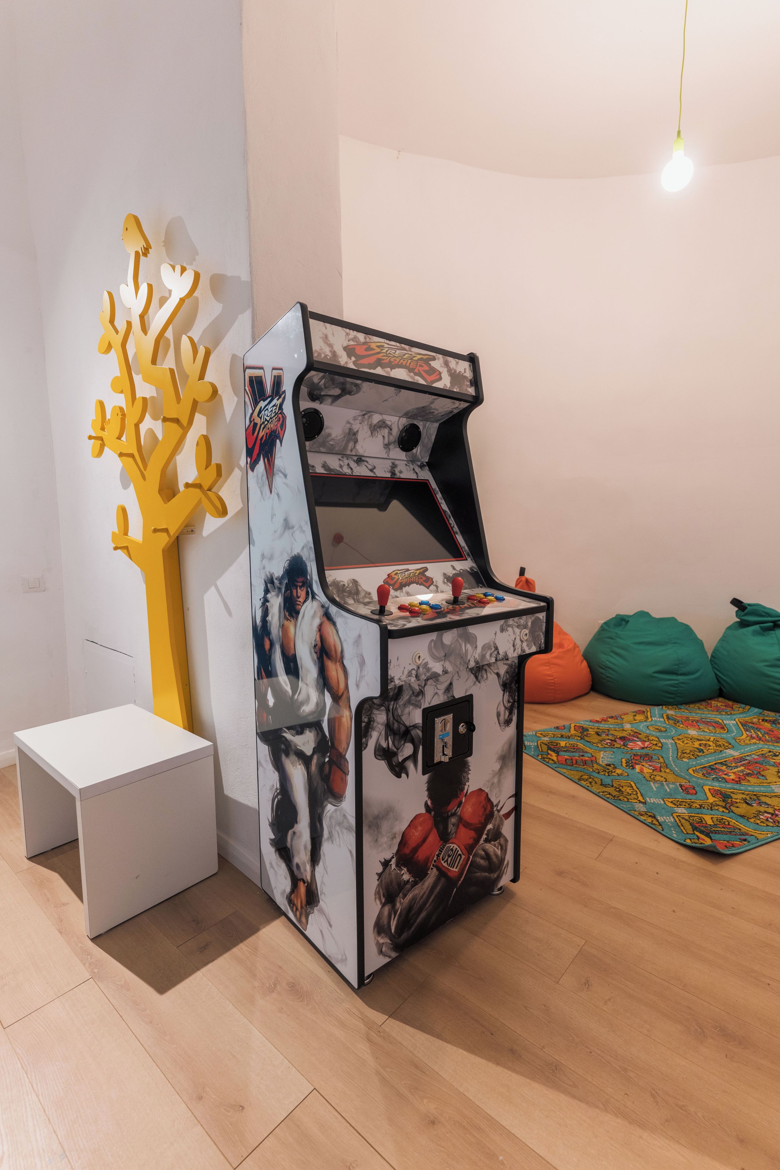 A retro arcade machine with a muscular character on the front, a white cabinet, and a yellow abstract sculpture to the left.