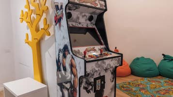 Una máquina de arcade retro con un personaje musculoso en la parte frontal, un gabinete blanco y una escultura abstracta amarilla a la izquierda.