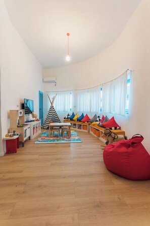 A cozy living room with a wooden floor, a red bean bag, a teepee, colorful cushions, a television, and a window with curtains. - 5chirpici (Murighiol)