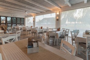 A spacious indoor dining area with large windows, white furniture, and a ceiling fan.