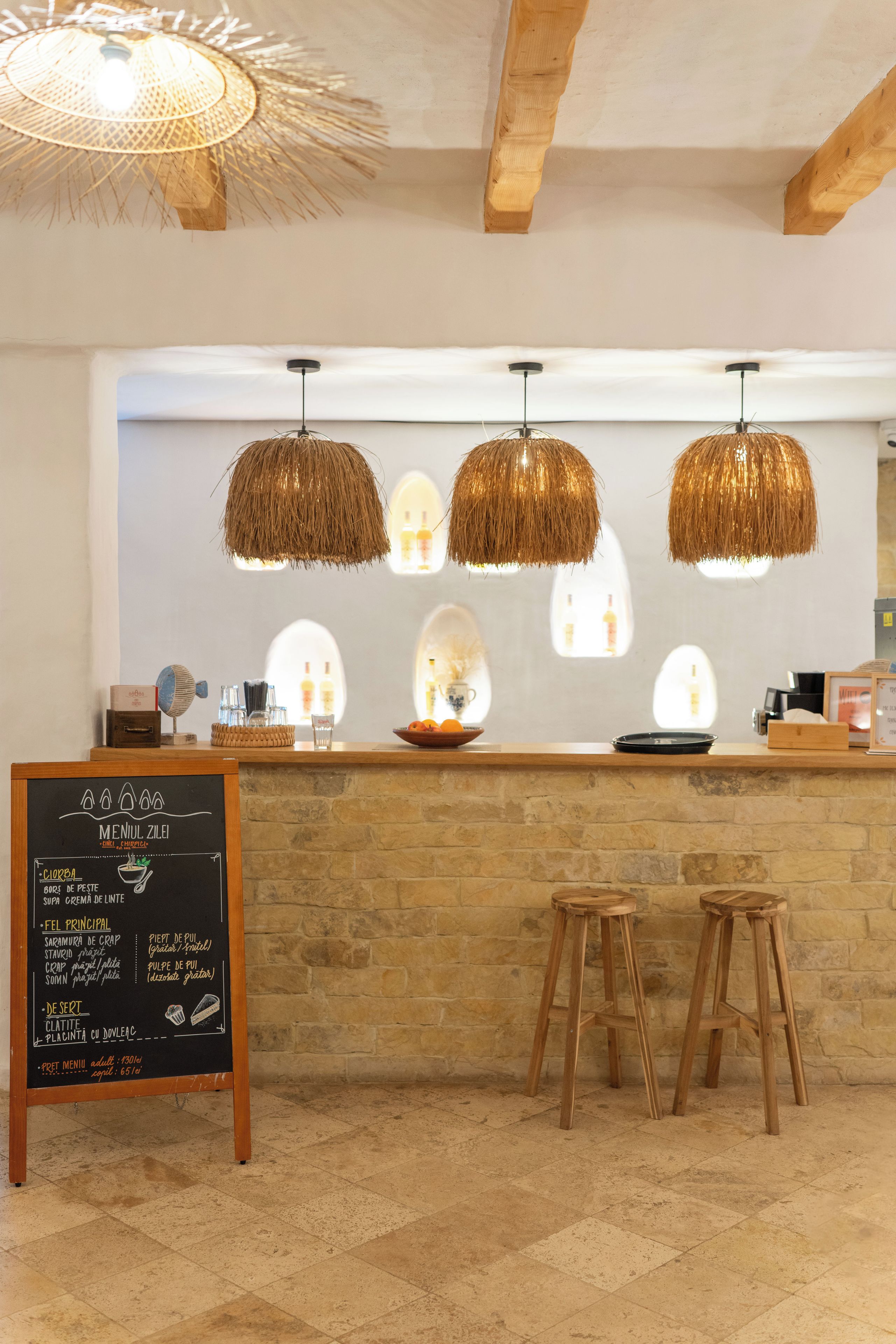 Ein Restaurantinneres mit einer Steintheke, drei hängenden Rattan-Kronleuchtern und einer Tafeln mit der Speisekarte.