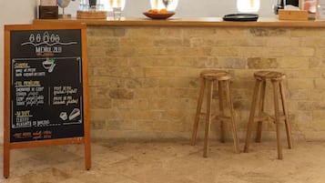 A restaurant interior with a stone counter, three hanging rattan chandeliers, and a chalkboard menu.