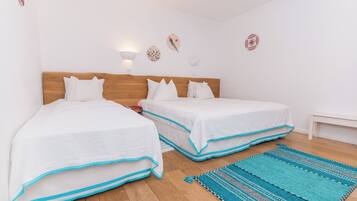A bedroom with two beds, wooden headboards, white bedding, and a blue patterned rug.