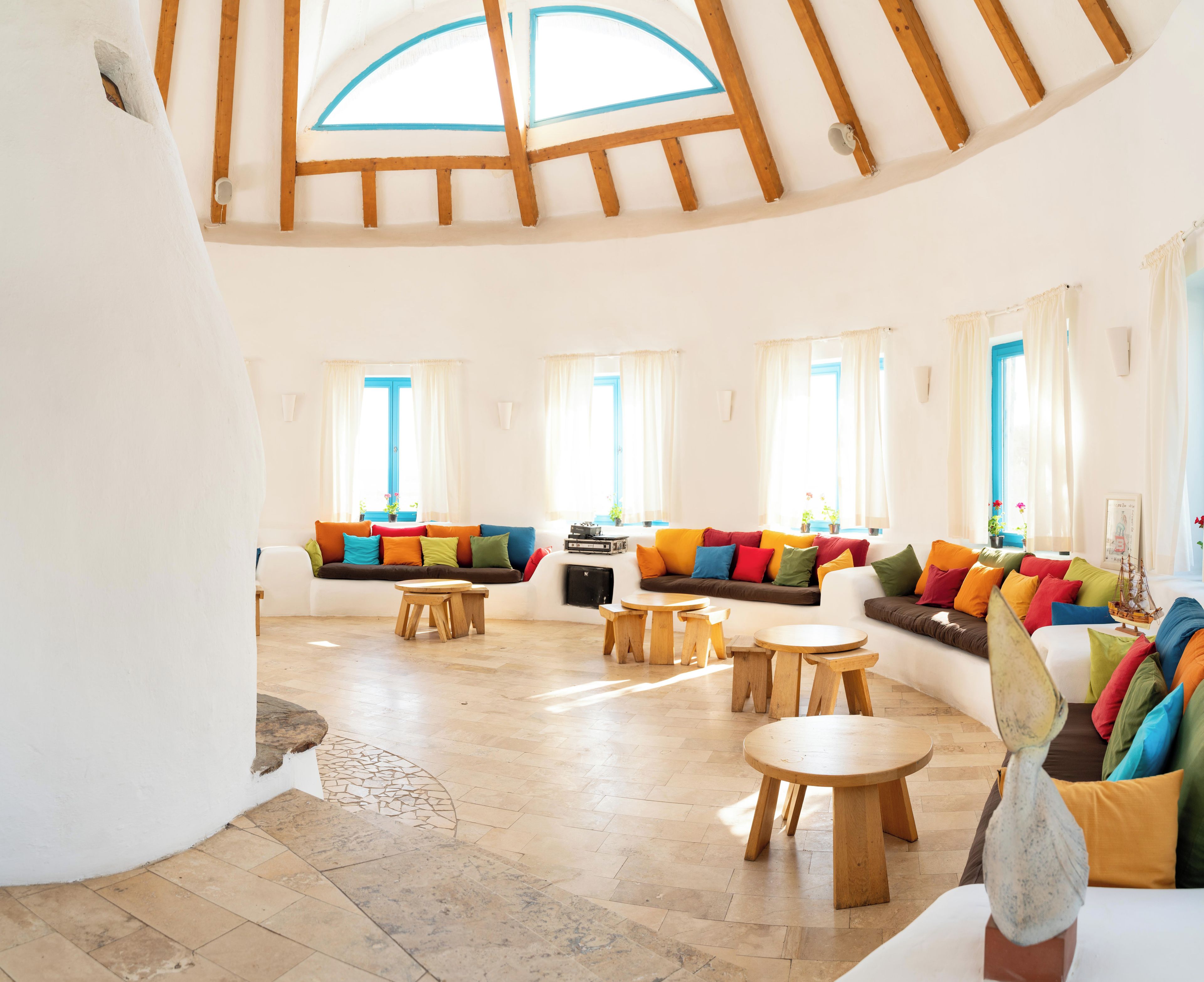 Amplia sala de estar con techo alto, vigas de madera, tragaluz circular, un conjunto de sofá colorido y una pequeña mesa de madera.
