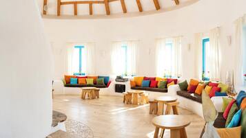 Amplia sala de estar con techo alto, vigas de madera, tragaluz circular, un conjunto de sofá colorido y una pequeña mesa de madera.
