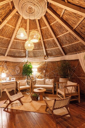 A thatched-roof room with wicker furniture, a woven ceiling light, and a central plant. - 5chirpici (Murighiol)