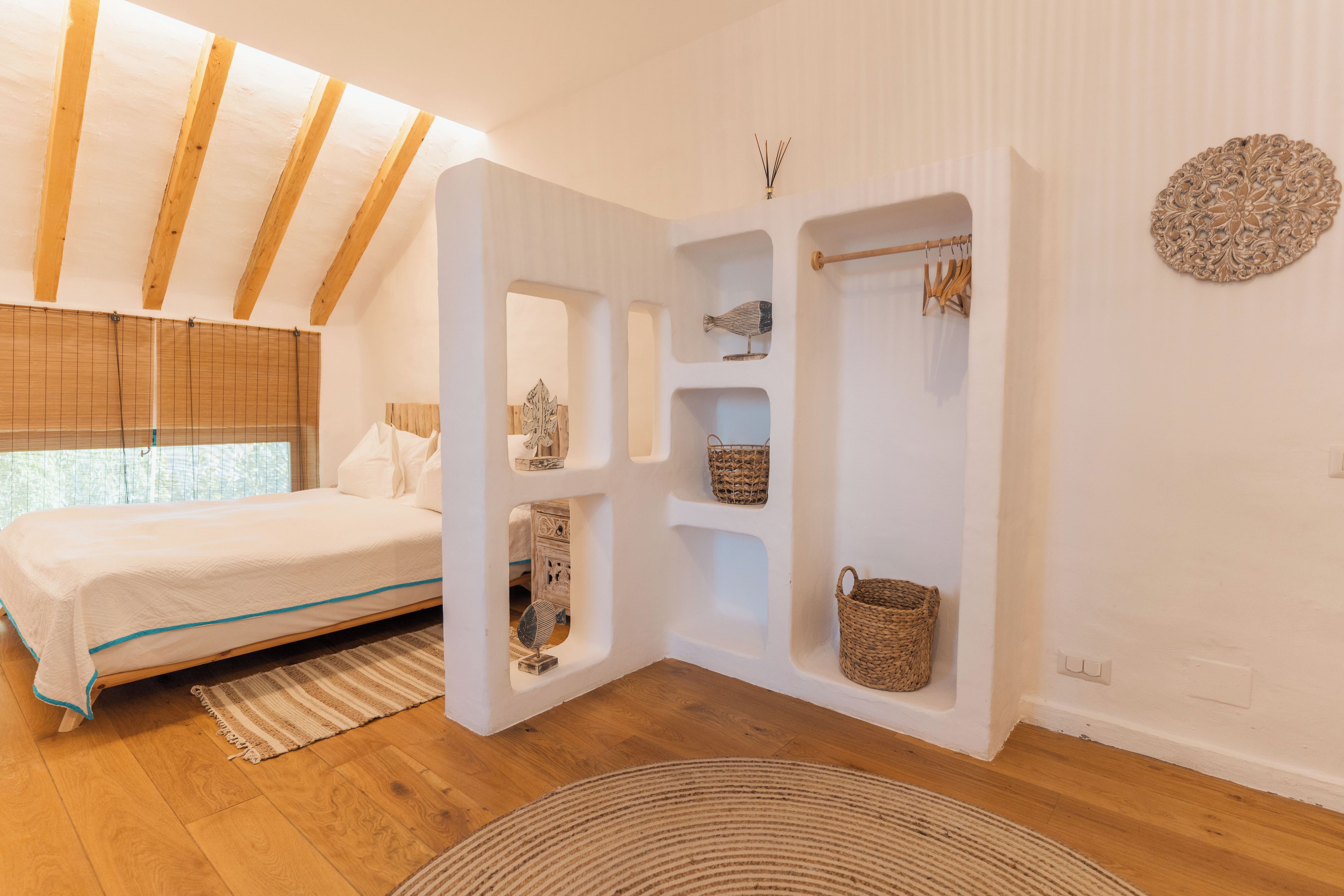 Un dormitorio con cama, vigas de madera, estante empotrado con cestas y un adorno de pared.