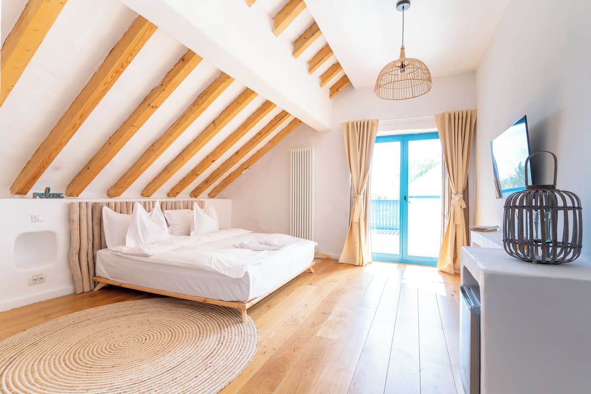 A bedroom with a sloped ceiling, a bed, a round rug, a television, and a window with curtains.