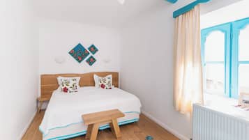 A bedroom with a wooden bed, a small bedside table, a window with curtains, and a wall-mounted light fixture.