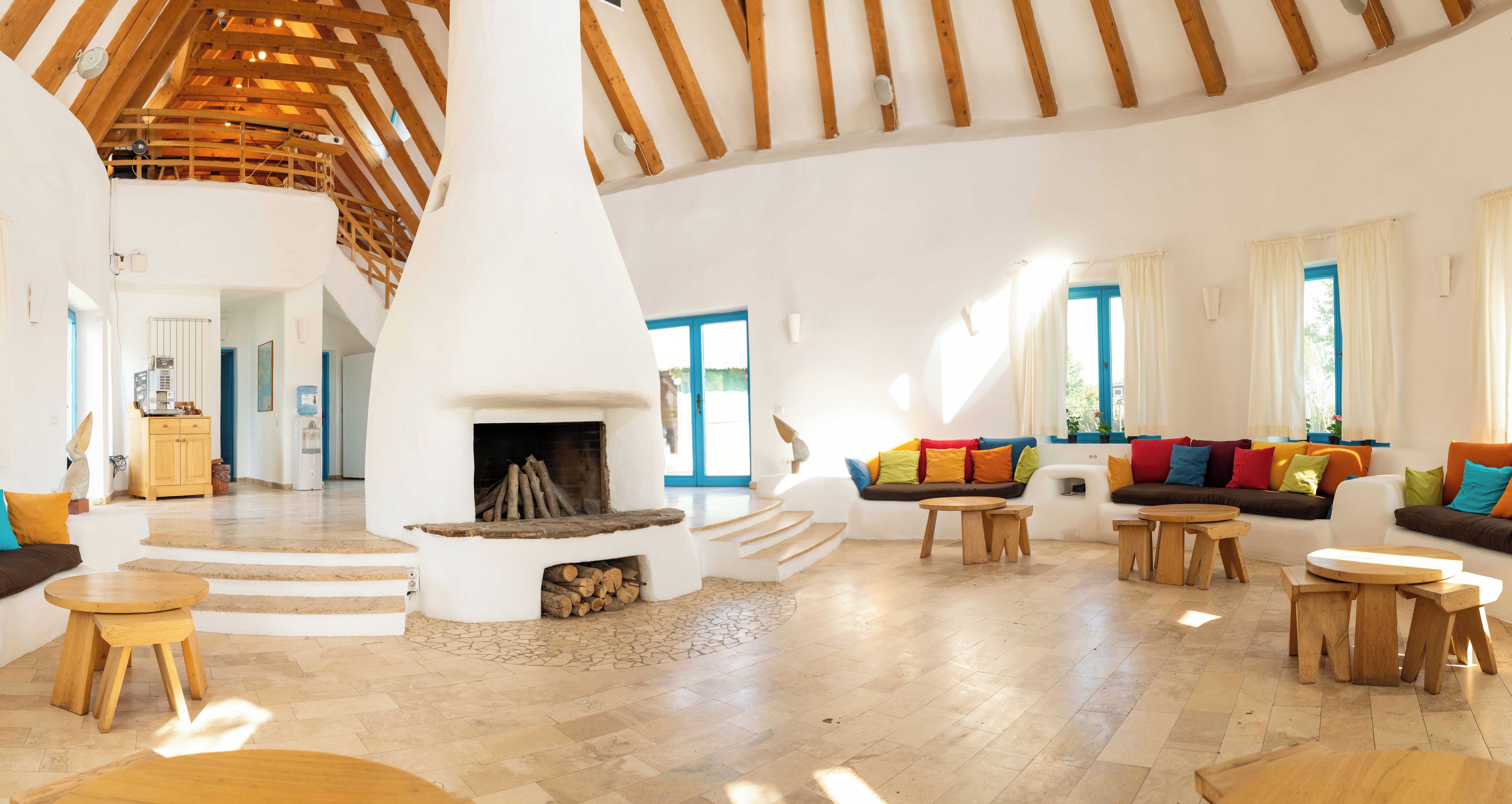Amplia sala de estar con chimenea central, muebles de madera y una escalera que lleva a un nivel superior.