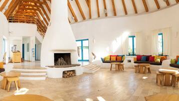 Amplia sala de estar con chimenea central, muebles de madera y una escalera que lleva a un nivel superior.