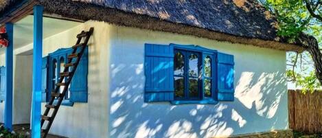 A house with a thatched roof, blue shutters, and a stone foundation.