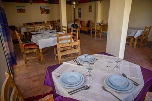Un restaurante con varias mesas dispuestas para comer, sillas de madera y suelo de baldosas.