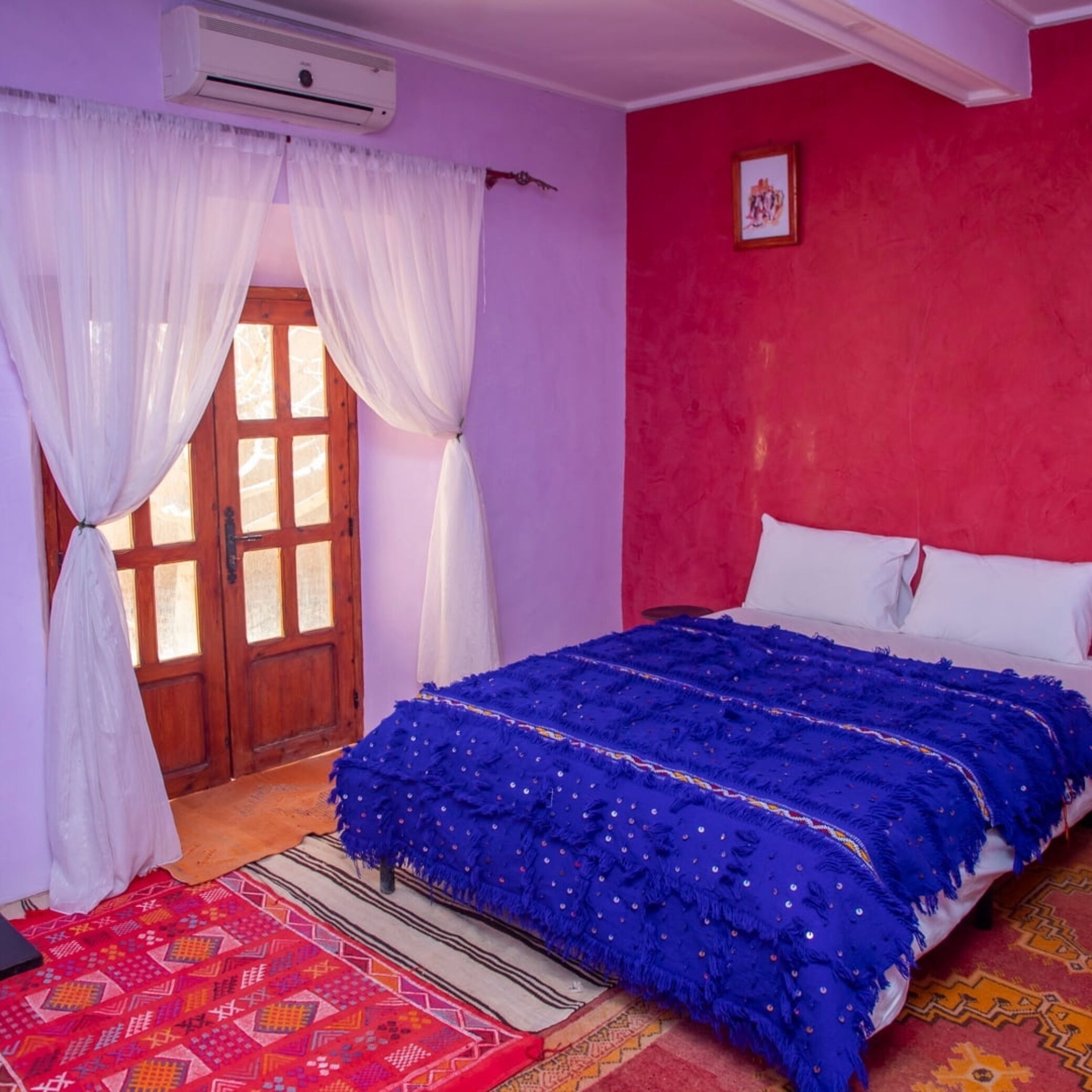 A bedroom with a bed, curtains, a red wall, and a door.