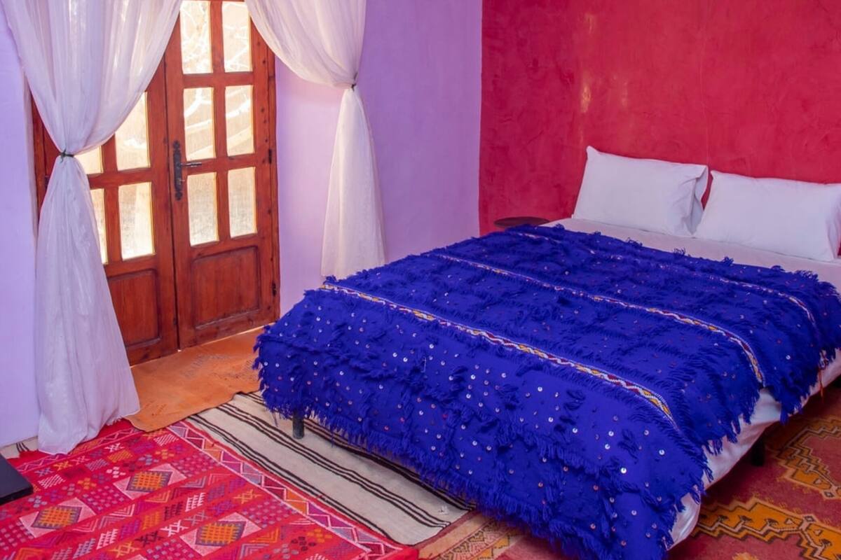 A bedroom with a bed, curtains, a red wall, and a door.