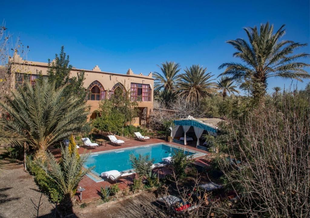 A pool area with lounge chairs, a building with arched windows, and palm trees.