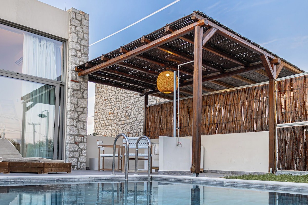 Une piscine avec un mur en pierre, une pergola en bois et une porte en verre.