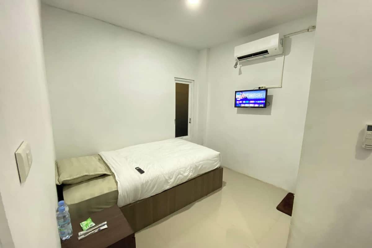 A small, clean room with a bed, a TV mounted on the wall, and an air conditioning unit.