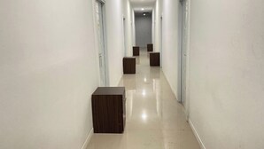 A long, narrow hallway with white walls and a shiny tiled floor. There are several doors on the left and right, and a few small wooden cabinets in the middle. - Medina House Syariah By Zuzu (Banda Aceh)