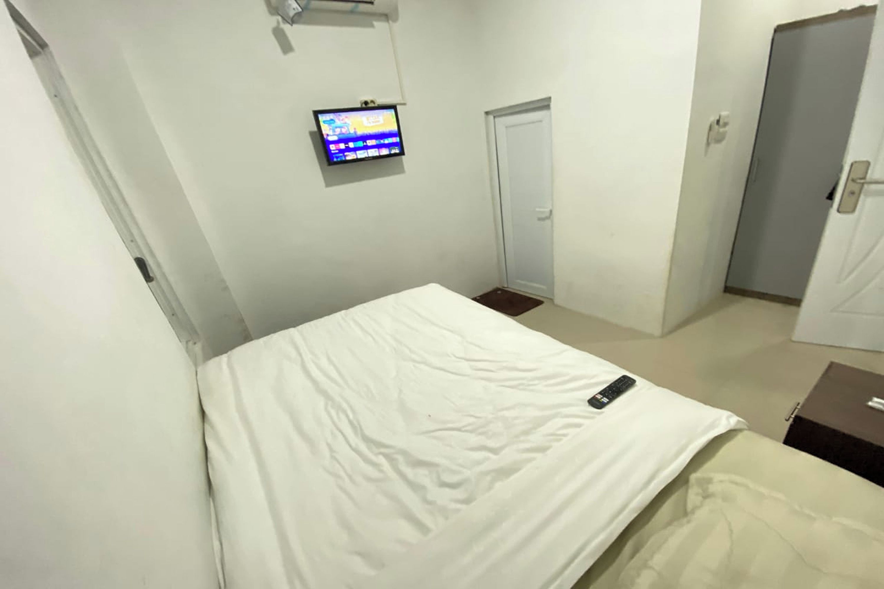A hotel room with a bed, a TV mounted on the wall, a door, and a small table.