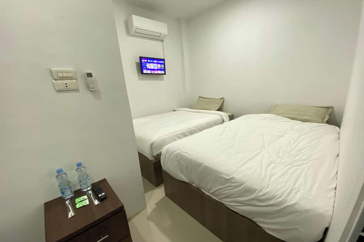 A hotel room with two beds, a TV, an air conditioner, a nightstand with a remote and water bottles.