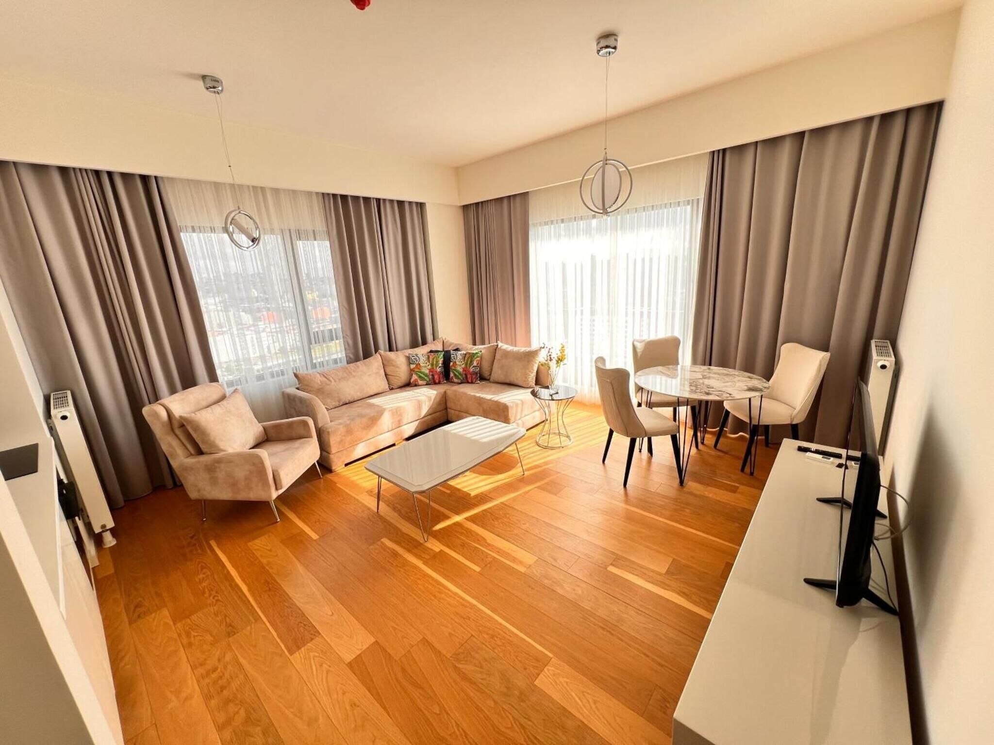 A modern living room with a sectional sofa, a coffee table, a dining table with chairs, and large windows with curtains.