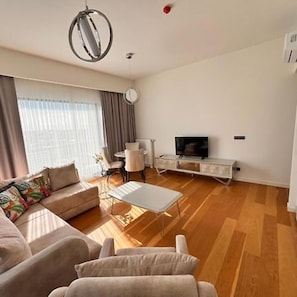 A modern living room with a sofa, coffee table, TV, and a dining area with chairs and a table. - Divan Residence Güneşli Near Mimar Sinan Metro St (Istanbul)