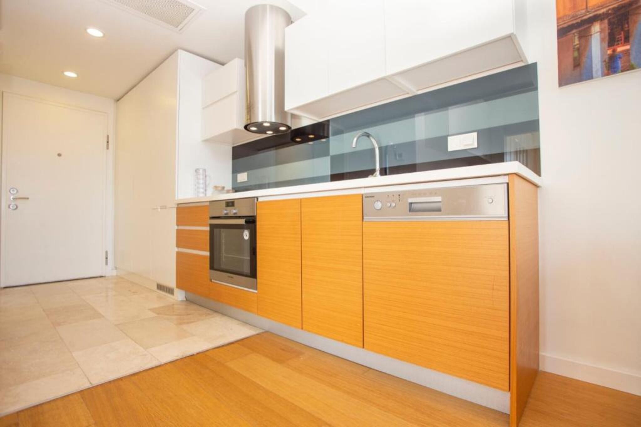 A modern kitchen with wooden cabinets, a stainless steel range hood, and a dishwasher.