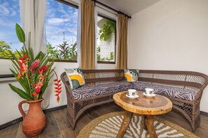 A wicker sofa with zebra-patterned cushions, a terracotta vase with red flowers, and a wooden coffee table. - Ecotica Boutique Hotel (Quepos)