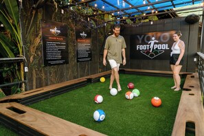 A recreational area with a pool table, surrounded by a netted enclosure, and a sign indicating 'Foot Pool' rules. - Ecotica Boutique Hotel (Quepos)
