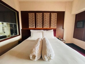 A hotel room with a large bed, a wooden headboard, a nightstand with a phone, and a window with a view. - I Lux Hotel Jogja (Ngaglik)