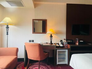 A hotel room with a desk, chair, bed, television, and a refrigerator. - I Lux Hotel Jogja (Ngaglik)