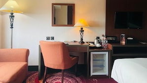 A hotel room with a desk, chair, bed, television, and a refrigerator. - I Lux Hotel Jogja (Ngaglik)