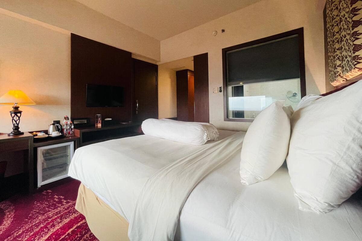 Une chambre d’hôtel avec un lit, une télévision, un bureau avec une lampe et une fenêtre.