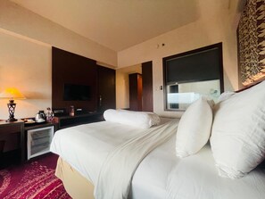 Et hotelværelse med en seng, fjernsyn, et skrivebord med lampe og et vindue.
