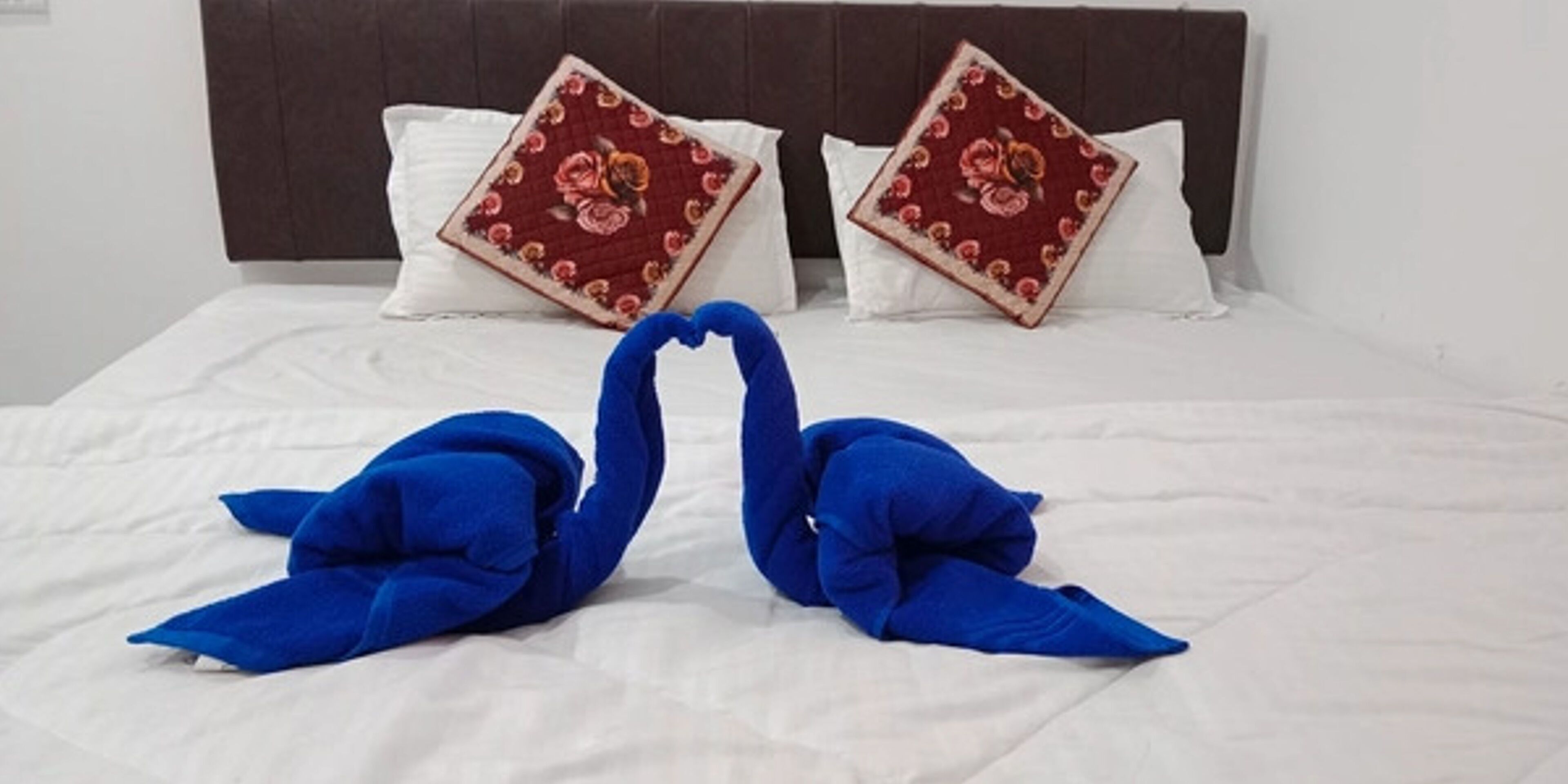 Una cama con ropa de cama blanca, dos almohadas con diseños florales y dos toallas con forma de cisne azules.