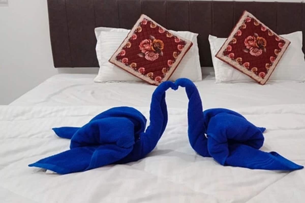 A bed with white bedding, two pillows with floral patterns, and two blue swan-shaped towels.