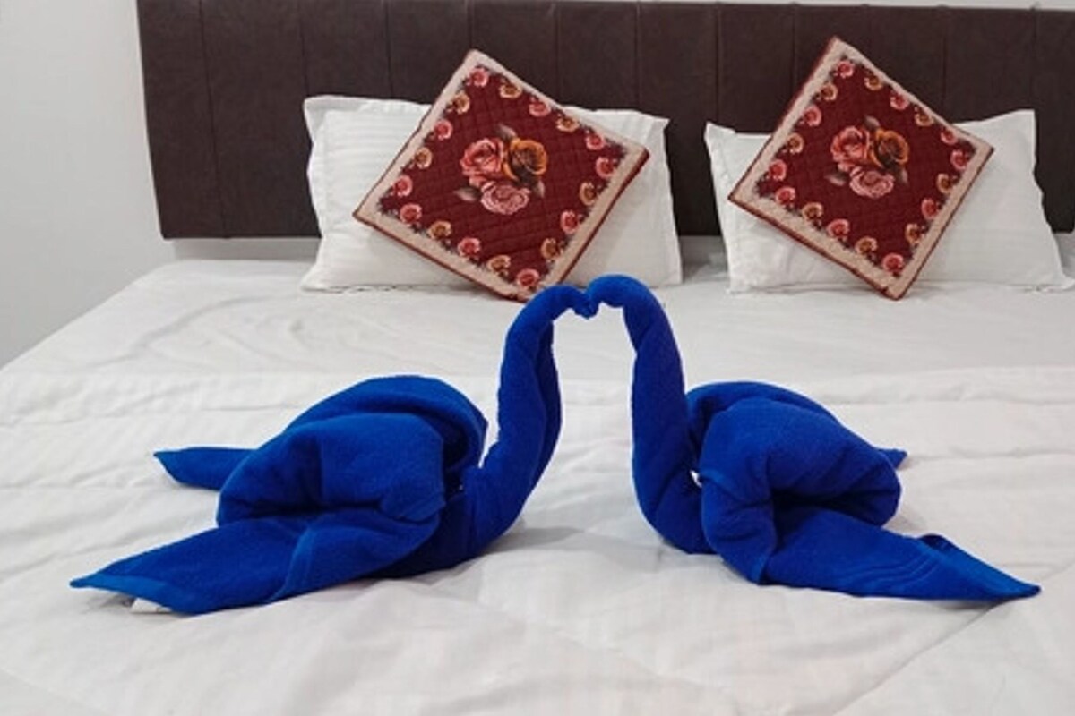 A bed with white bedding, two pillows with floral patterns, and two blue swan-shaped towels.