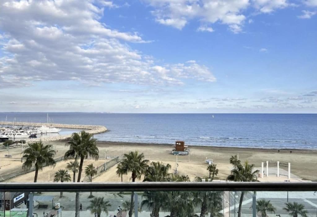 Vista de una playa con palmeras, un muelle y un pequeño edificio sobre la arena.