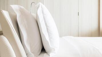 Una cama bien hecha con ropa de cama y almohadas blancas, un armario de madera al fondo y una puerta a la derecha.