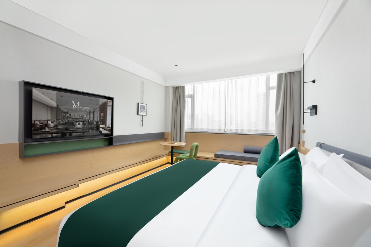 Et hotelværelse med seng, siddeplads, tv og et vindue med gardiner.