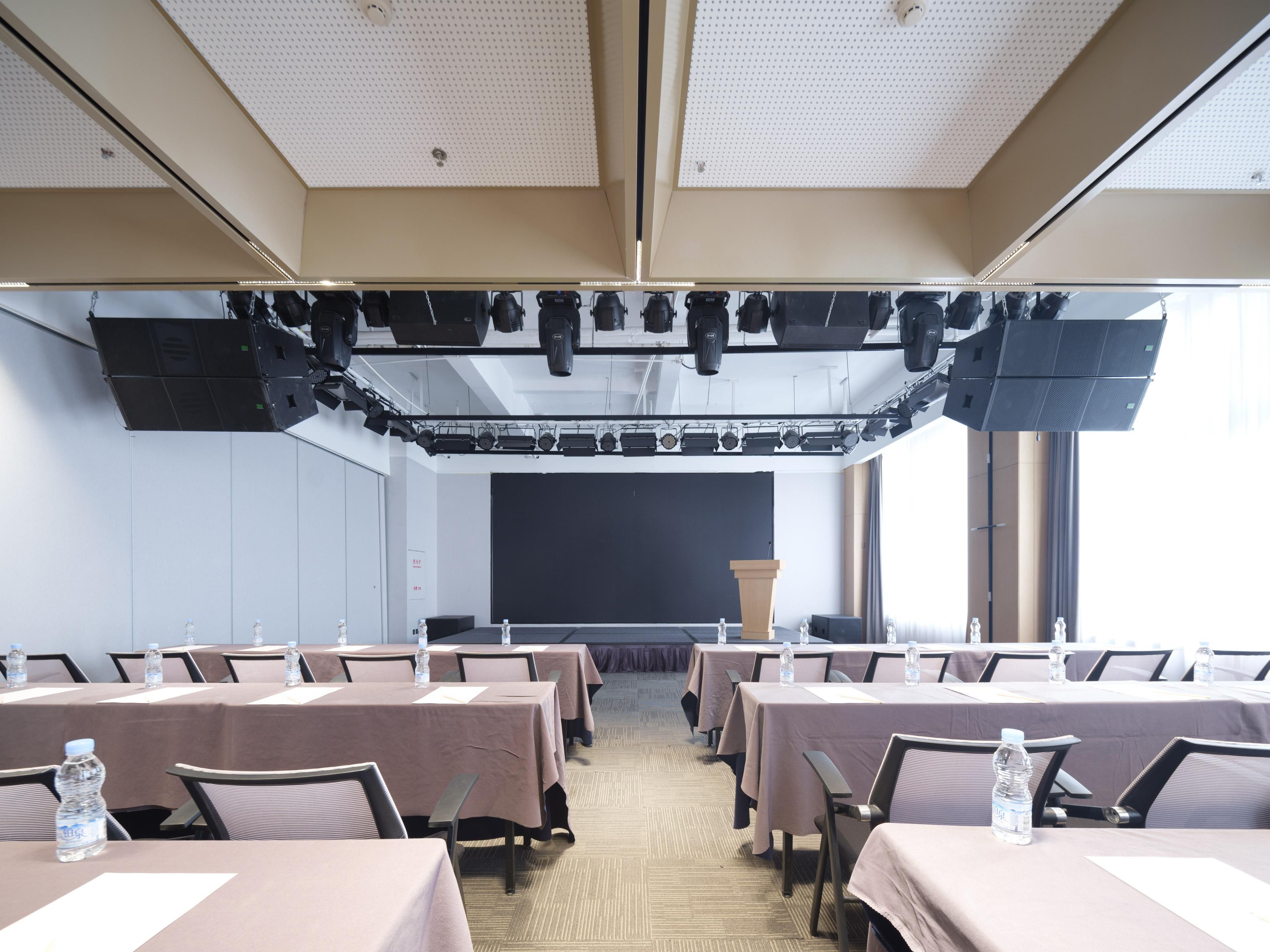 Un salón de conferencias con mesas, sillas, un atril y una pantalla grande.