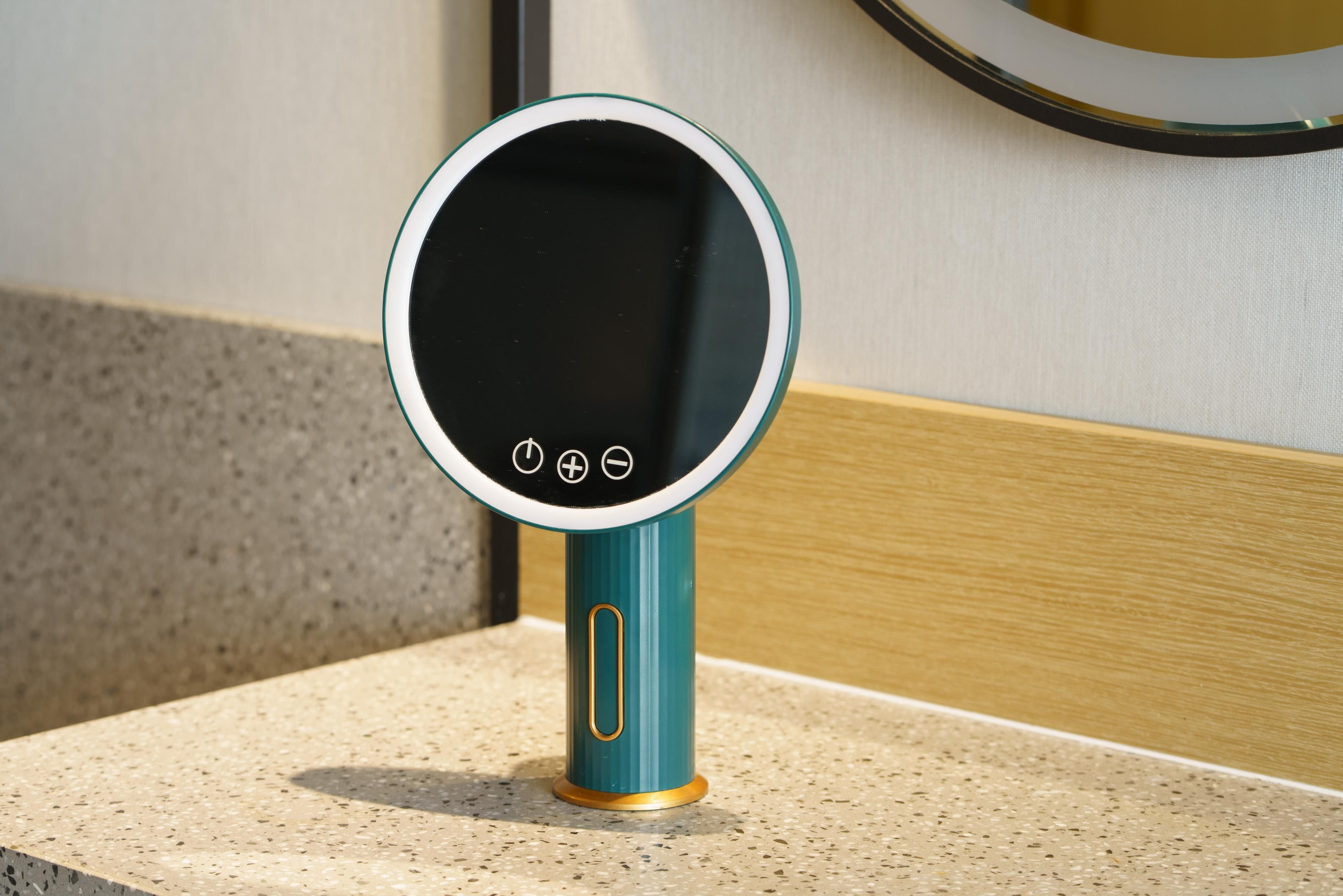 A teal and gold digital mirror with a circular frame, mounted on a textured beige countertop.